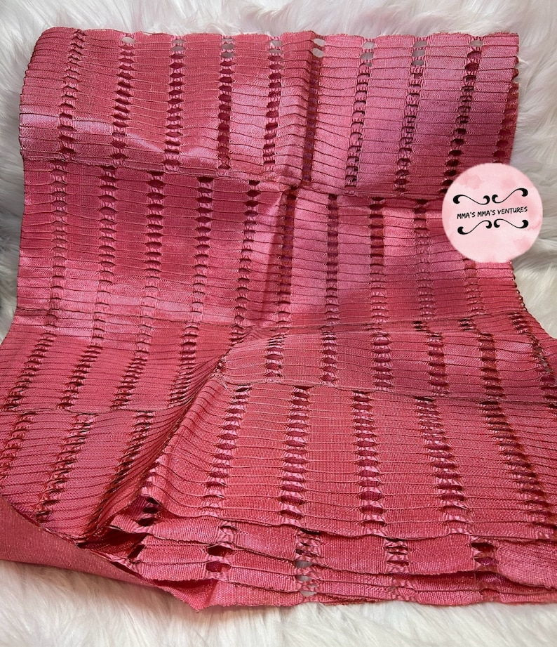 以下が含まれることがあります： ピンク色の、テクスチャ加工されたリブ編みデザインの折り畳まれた布。 垂直に切り抜かれた部分があり、重ね着のような効果を生み出しています。 素材はわずかに光沢があるように見えます。 画像には「mma's mma's ventures」というテキストが入った円形のロゴが含まれています。