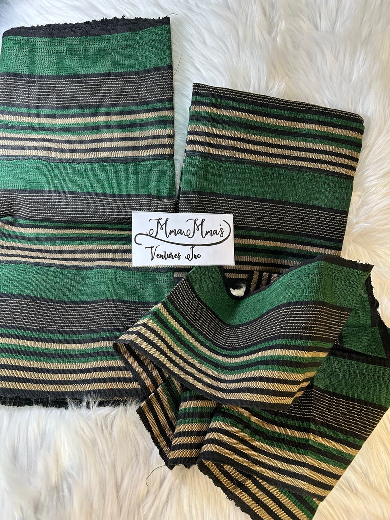 May include: Striped fabric in green, black, and beige colors. The fabric is folded and arranged on a white fluffy surface. The text "Mmau Mma's Ventures Inc" is visible on a white label.