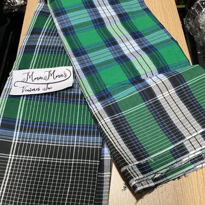 May include: Two folded plaid fabric pieces in green, blue, black, and white. One piece has a grid pattern in black and white. The other piece has a green, blue, and white plaid pattern. The text "Mman Mma's Ventures Inc" is visible.