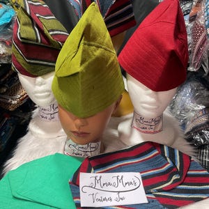 May include: A collection of colorful, patterned hats displayed on mannequin heads. The hats are in various colors, including red, green, and striped patterns. The text "Mmare Mma's Ventures Inc" is visible on a label.