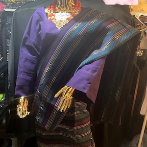 May include: A purple and black striped fabric with gold accents. The fabric is draped over a mannequin wearing a purple top and a matching head wrap. The text "MMA's MMA's Ventures African Finest Clothing For All" is visible in the image.