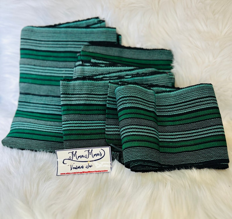 May include: A stack of five green and black striped fabric strips. The fabric is woven with a textured pattern. The strips are folded and stacked on a white fuzzy surface. A small white tag with the text "Mama Mais Ventures Inc. www.etsy.com/shop/MamaMaisVenturesInc" is in the lower left corner of the image.