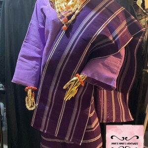 May include: A purple and white striped fabric with a matching head wrap. The fabric is draped over a gold mannequin. The mannequin is wearing a purple top and a necklace with red beads. The text "MMA'S MMA'S VENTURES" is visible in the bottom right corner of the image. The text "African Finest Clothing For All" is also visible.