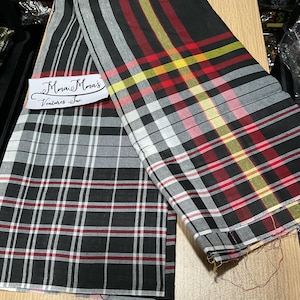 May include: Two plaid fabric pieces, one black and white, the other black with red, yellow, and white stripes. The fabric is folded on a wooden surface. A label reads "Mma's Ventures Inc."
