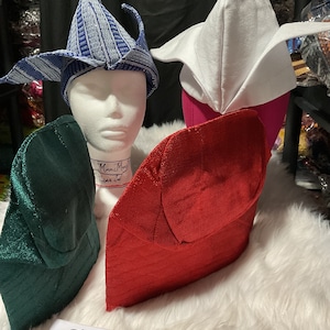 May include: A collection of colorful, textured hats in various styles. The hats include a blue and white patterned hat, a white hat, a red hat, and a green hat. The hats are displayed on mannequin heads.