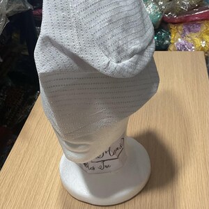 May include: A light gray, textured hat displayed on a white mannequin head. The hat has a slight sheen and a horizontal striped pattern. A small white card with "Option F" is in front of the mannequin.