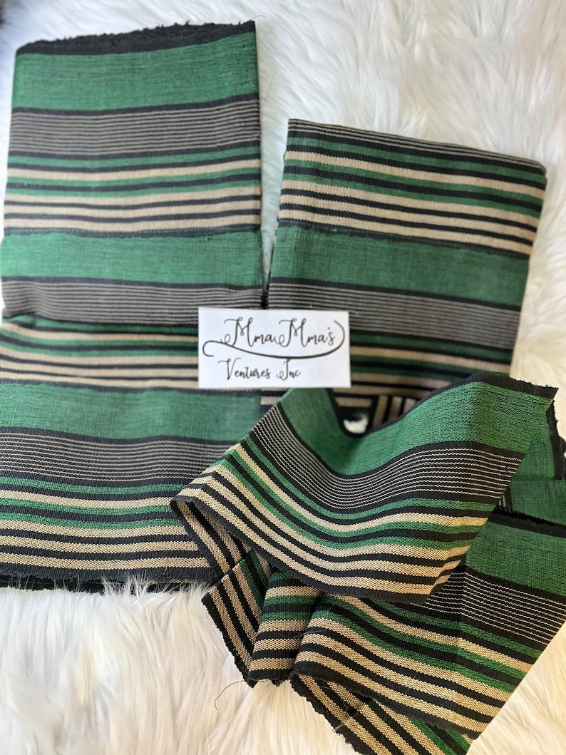 May include: Two pieces of green, black, and beige striped fabric. The fabric is folded and has a frayed edge. The fabric is labeled "Mmau Mma's Ventures Inc."
