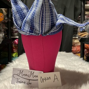 May include: A blue and white patterned head wrap, displayed on a pink mannequin head. The head wrap has a triangular shape with folded edges. A card reads "Option A" and another card reads "Mmare Mma Ventures Inc."