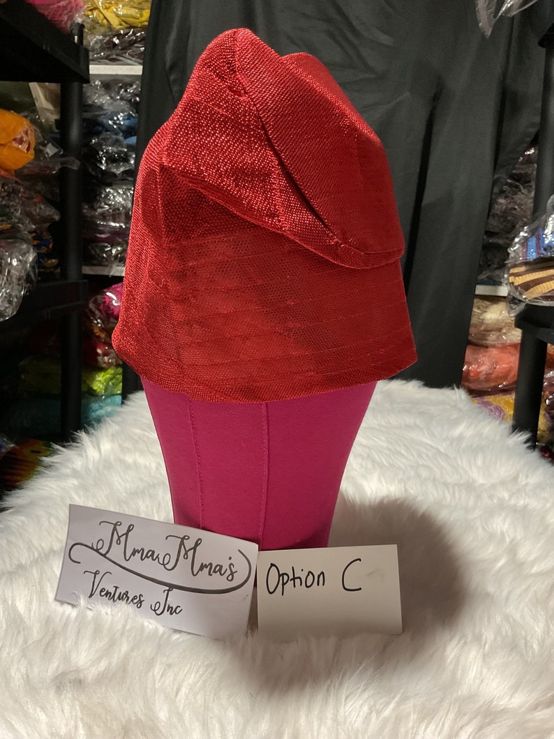 May include: A vibrant red hat with a textured surface, displayed on a pink mannequin head. The hat has a unique folded brim. The text "Option C" is visible on a white card. The hat is part of the "Mma's Ventures Inc" collection.