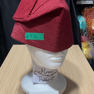 May include: A red fabric hat with a folded brim, displayed on a white mannequin head. The hat has a textured appearance. A green sticker indicates a measurement of 23 1/2 inches. A label below reads "Option E."