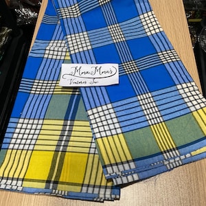 May include: A folded blue, yellow, and white plaid fabric. The fabric has a repeating pattern of intersecting lines. The text "Mma Mma's Ventures Inc" is printed on a white label.
