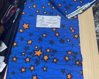 May include: Blue fabric with a pattern of orange and black stars on a blue background with thin black lines. The fabric is folded in half and the text "Minnie Mais Ventures LLC" is visible on a white tag.