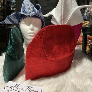 May include: An assortment of colorful, textured hats in various designs. The hats include a blue and white striped hat, a white hat with pink accents, a red hat, and a green hat. The hats are displayed on a white surface.