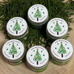 Könnte beinhalten: Sechs kleine Glasgefäße mit grüner Flüssigkeit und weißen Deckeln. Die Deckel haben ein Weihnachtsbaumdesign mit dem Text "frohe Weihnachten" und "Tannenbaum- Bausatz".