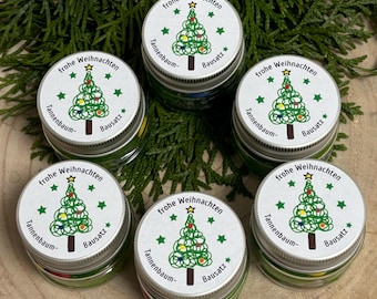 Puede incluir: Seis pequeños frascos de vidrio con líquido verde y tapas blancas. Las tapas tienen un diseño de árbol de Navidad con el texto "frohe Weihnachten" (Feliz Navidad) y "Tannenbaum- Bausatz" (kit de árbol de Navidad).