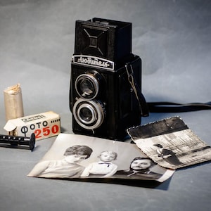 May include: A vintage black twin-lens reflex camera with a leather strap, film roll, and a box of film labeled "ФОТО 250" are displayed with two black and white photographs. The camera has a silver lens ring.