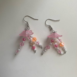 May include: Pink and white beaded earrings with a pink flower charm. The earrings have a silver hook.