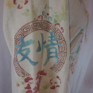 May include: Cream-colored fabric with a floral pattern and a circular design containing Chinese characters. The flowers are red, pink, and yellow. The text is in blue. The circular design is brown.