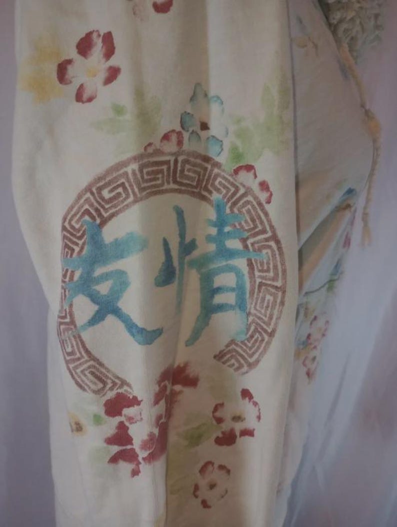 May include: Cream-colored fabric with a floral pattern and a circular design containing Chinese characters. The flowers are red, pink, and yellow. The text is in blue. The circular design is brown.