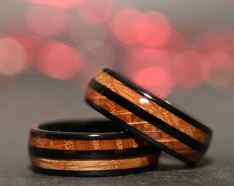 May include: Two black and brown wooden rings with black inlay. The rings are stacked on top of each other. The background is blurred and out of focus.