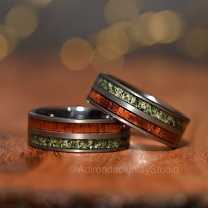 May include: Two matching wedding bands with a silver metal base and inlaid strips of wood and green stone.