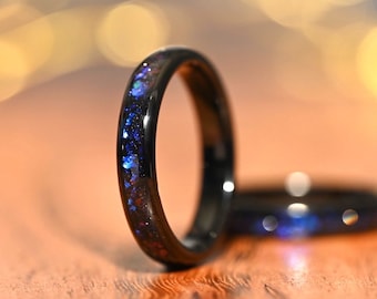 May include: Black ceramic ring with a thin band of blue and purple glitter embedded in the resin. The ring is shown on a wooden surface.