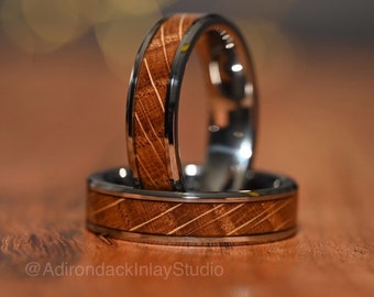 May include: Two wedding bands with a wood inlay design. The bands are made of stainless steel and have a brown wood inlay. The wood inlay has a striped pattern.