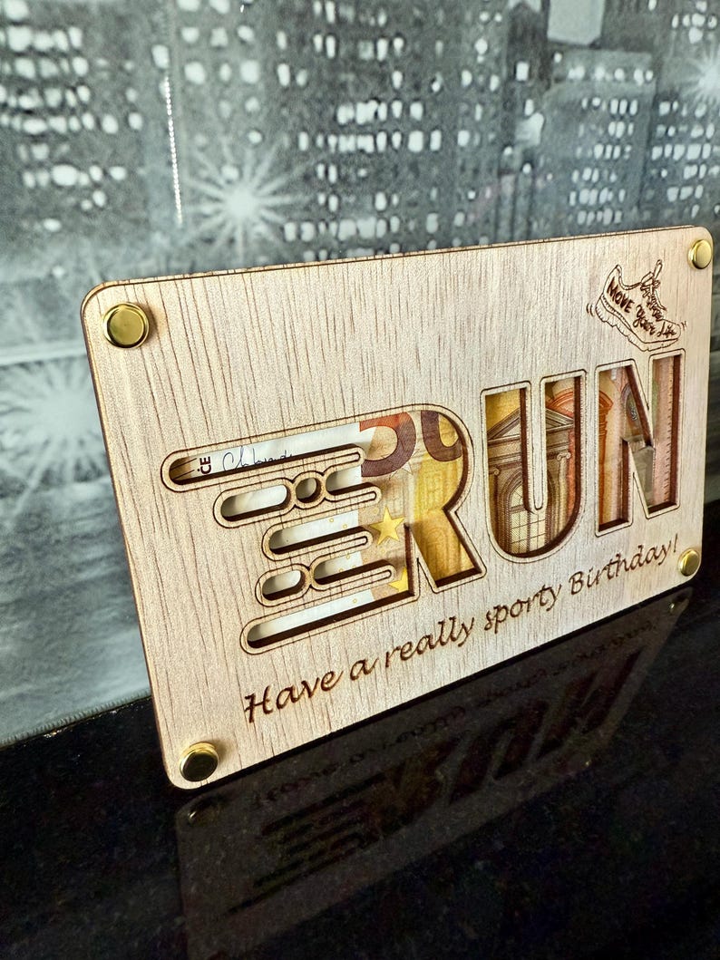 May include: Wooden plaque with the word "RUN" cut out, revealing currency inside. The plaque has the text "Have a really sporty Birthday!" and a small shoe graphic. Gold-colored rivets secure the corners.