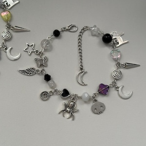 May include: A silver charm bracelet with a variety of charms, including a crescent moon, a star, a butterfly, a spider, a skull, a heart, and a spiral. The bracelet also has black and clear beads.