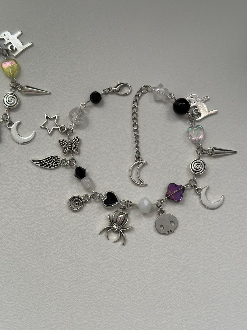 May include: A silver charm bracelet with a variety of charms, including a crescent moon, a star, a butterfly, a spider, a skull, a heart, and a spiral. The bracelet also has black and clear beads.