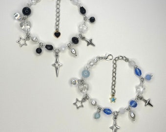 May include: Two silver charm bracelets with different colored beads. One bracelet has black beads and a silver heart charm, the other has blue beads and a silver star charm.
