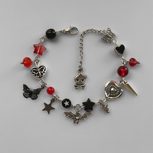 May include: A silver charm bracelet with red and black beads, charms include stars, hearts, butterflies, a skull, a bat, and a spike.