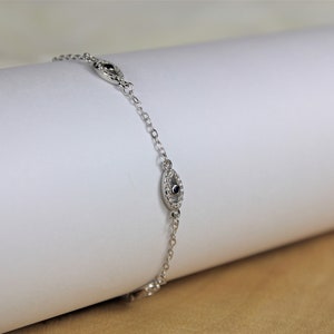 May include: A silver chain bracelet with three small, oval-shaped charms. Each charm has a black stone in the center and is surrounded by smaller white stones.