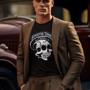 Könnte beinhalten: Ein Mann in braunem Anzugjackett und Hose, einem schwarzen T-Shirt mit einem weißen Totenkopf-Motiv und dem Text "Sinister Urge", einer braunen Flatcap und einer Uhr am linken Handgelenk. Das T-Shirt trägt außerdem den Text "Baron Wallin Devil's Backbone, TX".