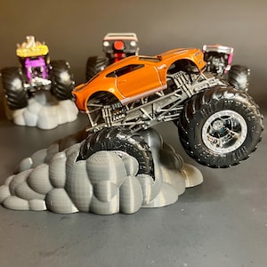 May include: Orange monster truck with large black wheels and a gray cloud base. The truck is a modified version of a Chevrolet Camaro.