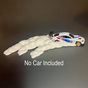 May include: A white toy race car with blue and red accents, number 87, sits on a white cloud-like structure. The text "No Car Included" is displayed below the objects. The car has a black spoiler and gold wheels.