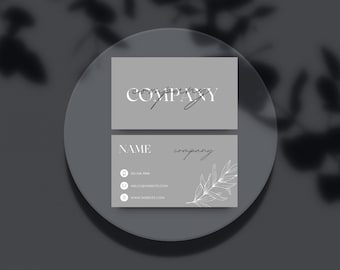May include: A gray business card with the text "company" in white, followed by a handwritten signature. The second card has the text "NAME" in white, followed by "company" in a handwritten font. The card also includes a white line drawing of a branch with leaves, a phone number, email address, and website address.