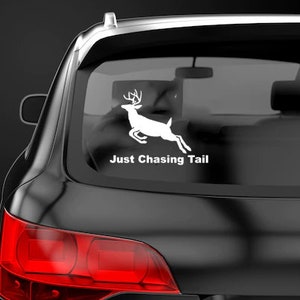 May include: A white vinyl sticker with a silhouette of a deer jumping and the text "Just Chasing Tail" on a black car.