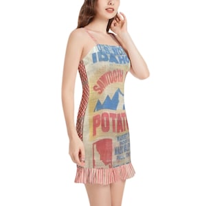 Puede incluir: Un vestido sin mangas con un diseño de saco de patatas vintage con las palabras "U.S. NO. 1 IDAHO" y "SAWTOOTH POTATOES" en azul y rojo. El vestido tiene un panel lateral a cuadros rojos y blancos y un dobladillo con volantes.