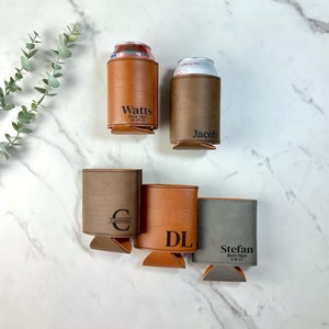 May include: Four personalized leather can coolers in brown, gray, and tan. The coolers are engraved with the names "Watts", "Jacob", "Cameron", and "Stefan" along with the text "Best Man" and the date.