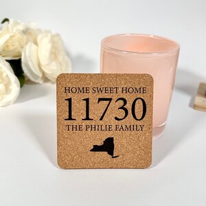 Op de afbeelding: Kurk onderzetter met de tekst "Home Sweet Home 11730 The Philie Family" en een zwart silhouet van de staat New York.
