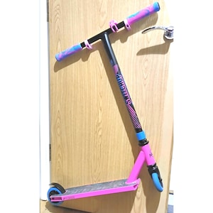 Puede incluir: Un patinete de acrobacias rosa y negro con empuñaduras de manillar y ruedas azules. El patinete tiene la palabra "SALTSTEP" impresa en la plataforma.