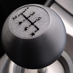 May include: A black gear shift knob with a standard 5-speed pattern.