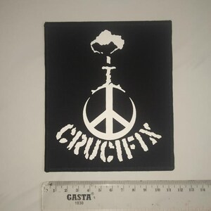 May include: Black and white patch featuring a peace sign and the word "CRUCIFY" in a stylised font.