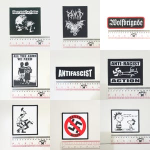 May include: A selection of nine black and white patches with diverse designs and text. The patches feature band logos, anti-fascist slogans, and illustrations. Each patch is approximately 7.6 cm in length.