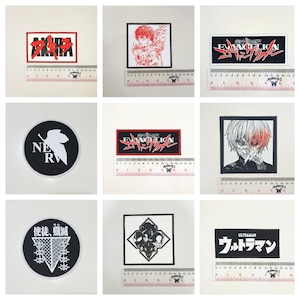 May include: Nine embroidered patches with anime and manga designs. The patches feature text and character illustrations in red, white, and black. Each patch is rectangular or circular, with a ruler below for size reference in centimetres.