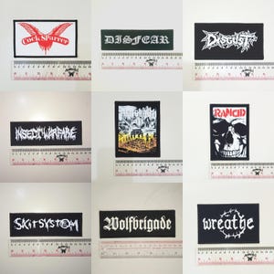 May include: A collection of nine rectangular patches with various band names and graphics. The patches feature text and images in white on a black background, with some including red and other colors. The patches are displayed on a white surface.