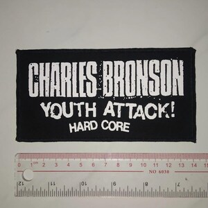 May include: Black and white embroidered patch with the text "CHARLES BRONSON YOUTH ATTACK! HARD CORE".