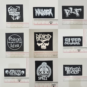 May include: Nine black and white iron-on patches with band names and logos. The patches include: "Naked Aggression", "Nausea", "P.L.F", "Poison Idea", "Rancid", "Sleep", "Spazz", "Spazz", and "Weekend Nachos".