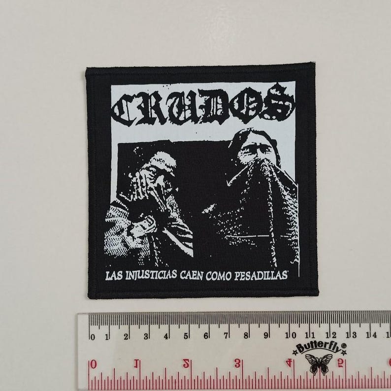 May include: Black and white patch with the text "CRUDOS" and "LAS INJUSTICIAS CAEN COMO PESADILLAS" in white lettering. The patch features two figures with their faces obscured.